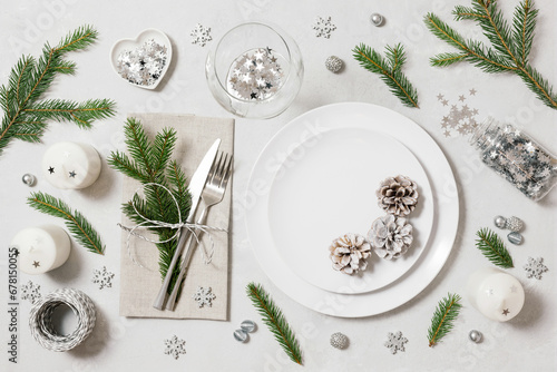 Festive table setting for Christmas dinner on white background. New Year serving with silver decor, fir branches and cones. View from above.