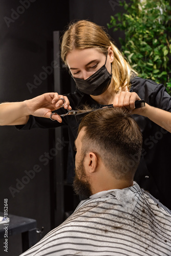 Woman hairdresser gives a haircut to a man in a barbershop. Male client looking in the mirror while getting a haircut. Step-by-step haircut. Vertical, Selective Focus, New Life, Male Style