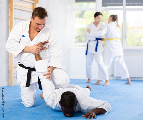 Sportive middle-aged man twisting his opponent's arm on the floor during judo classes