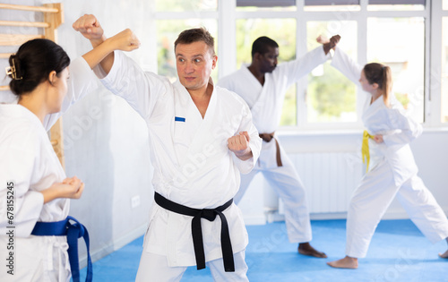 Adult man and young woman karatekas train karate in group in studio