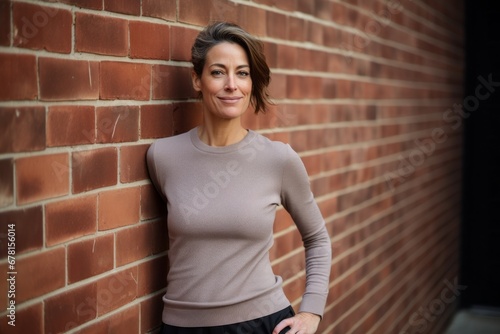 Portrait of a content woman in her 40s showing off a thermal merino wool top against a vintage brick wall. AI Generation © CogniLens