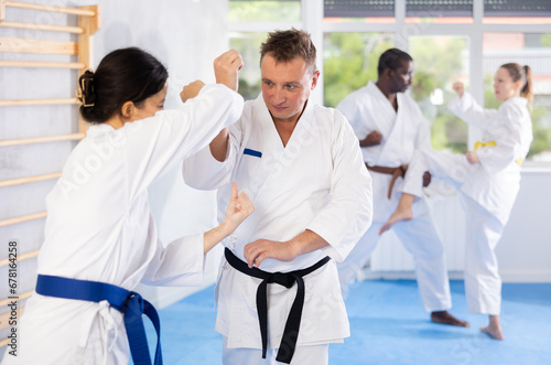 Woman and man in white kimono and belts sparring during karate training