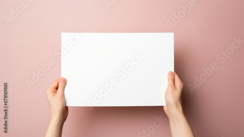 Female hands holding a blank white sheet of paper on a pink background.