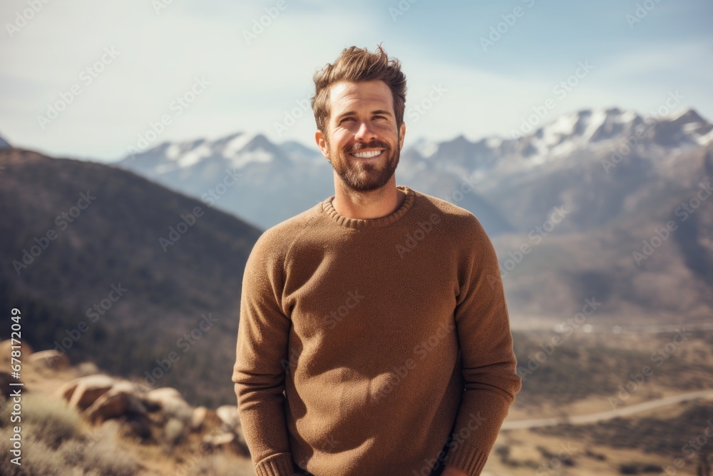 Portrait of a smiling man in his 30s wearing a cozy sweater against a panoramic mountain vista. AI Generation