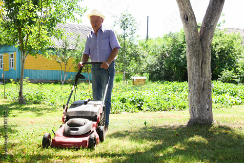 Elderly man with a lawn mower while mowing the lawn photo