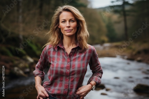 Portrait of a content woman in her 40s wearing a comfy flannel shirt against a tranquil forest stream. AI Generation
