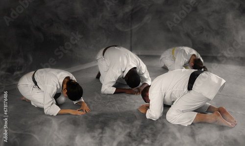 Teacher coach of martial arts and students followers sit on floor and make ritual obedience bows greet each other, thank one another for successful workout