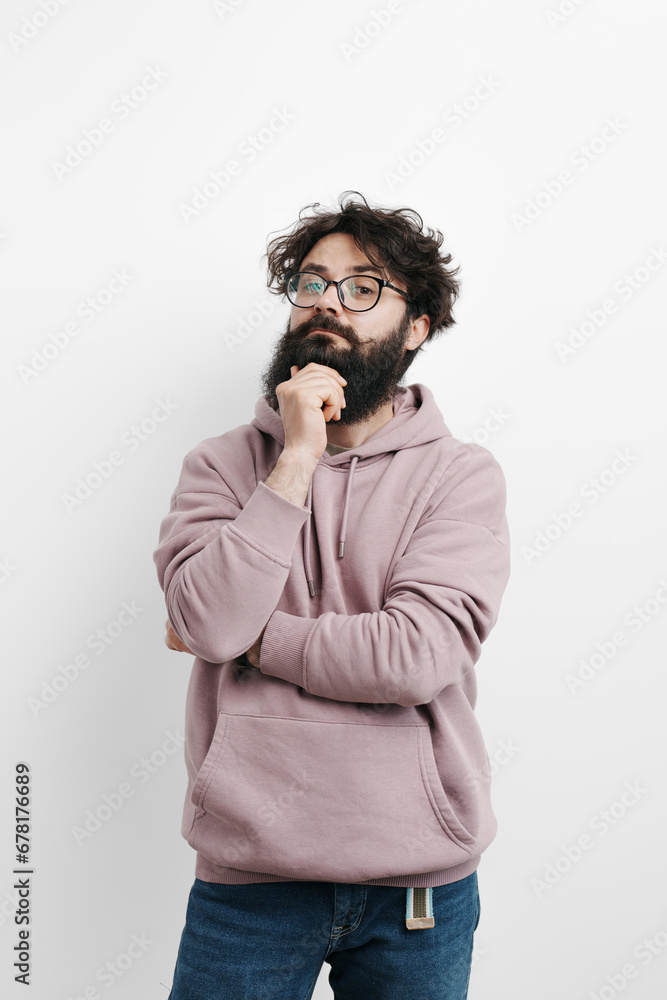 Pensive bearded man in glasses and a mauve hoodie, hand on chin, lost in thought against a clean white background