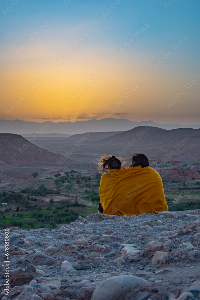 Two friends sharing a romantic moment under a blanket watching a sunset in the Sahara Desert