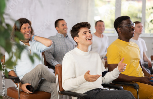 Group of young and middle aged men listening cheerfully to lecture sitting on chairs photo