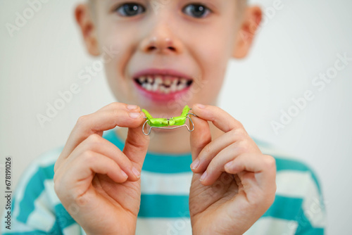 A blond-haired boy inserts orthodontic plate into his mouth to expand jaw and teeth. Close-up. Children's orthodontics, dental treatment, dentistry concept photo