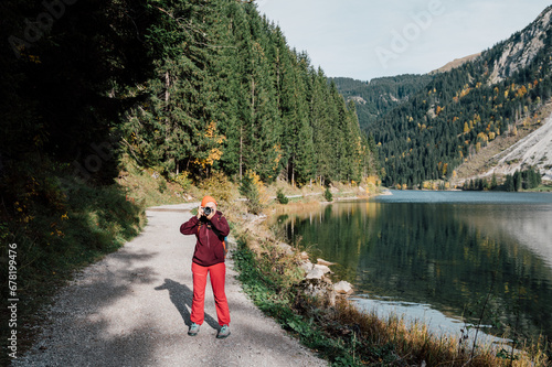 A photographer with a camera in his hands, wearing an orange hat, takes pictures in nature. near a lake in the mountains in the Alps