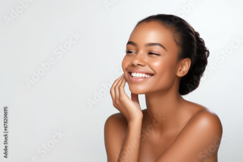 Portrait of a young smiling black woman touching her flawless glowy skin on soft white background, skincare concept photo