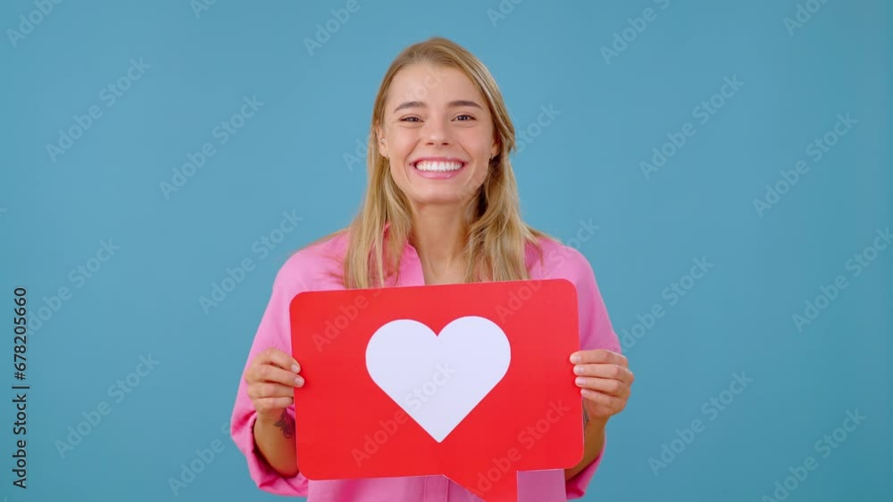 Cheerful woman smiles and shows red button with heart symbol Cheerful woman smiles and shows red button with heart symbol