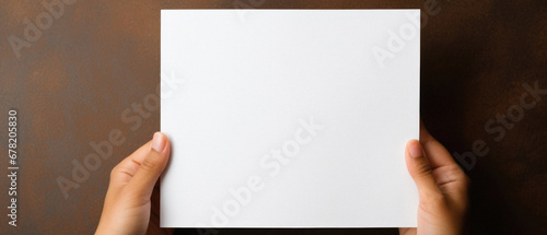 Hands holding blank paper sheet on brown background with copy space.