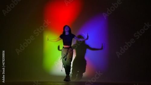 Attractive woman in top and black pants posing at camera dancing jazz funk in studio, isolated on red green blue neon background. © kinomaster