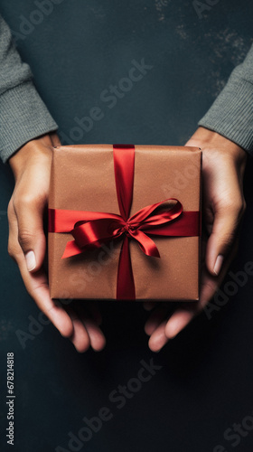 Female hands holding a gift box with red ribbon on dark background.
