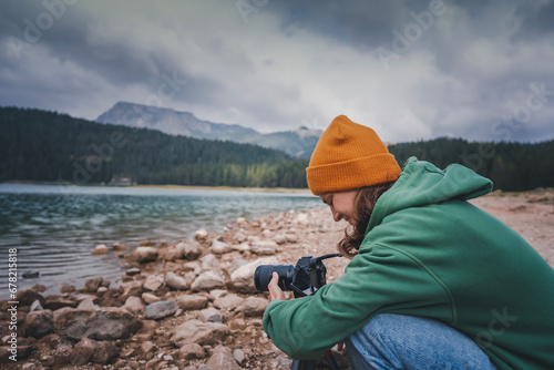 Young woman traveler hiker takes a photo using a camera on the shore of a mountain lake