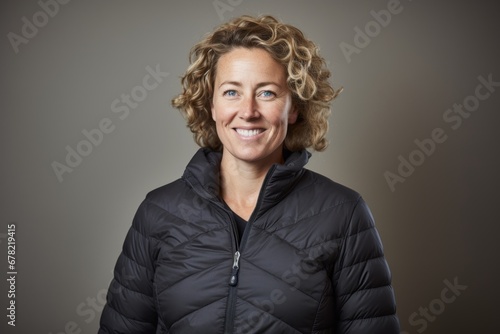 Portrait of a smiling woman in her 40s sporting a quilted insulated jacket against a plain cyclorama studio wall. AI Generation