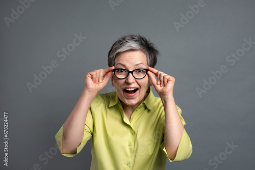 surprised 50s elderly woman by incredible discounts in green friday sales on studio grey background photo