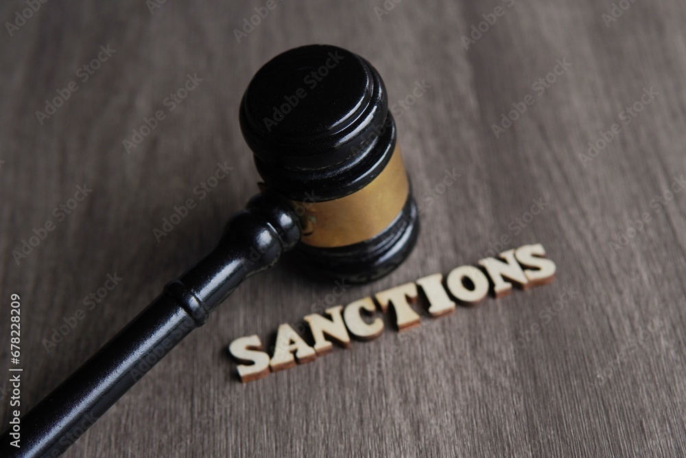 Close up image of judge gavel and text SANCTIONS on wooden table.