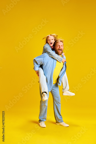 Father and daughter have fun. Dad giving piggyback ride to kid, teenager sit on back isolated on plain vivid yellow background.