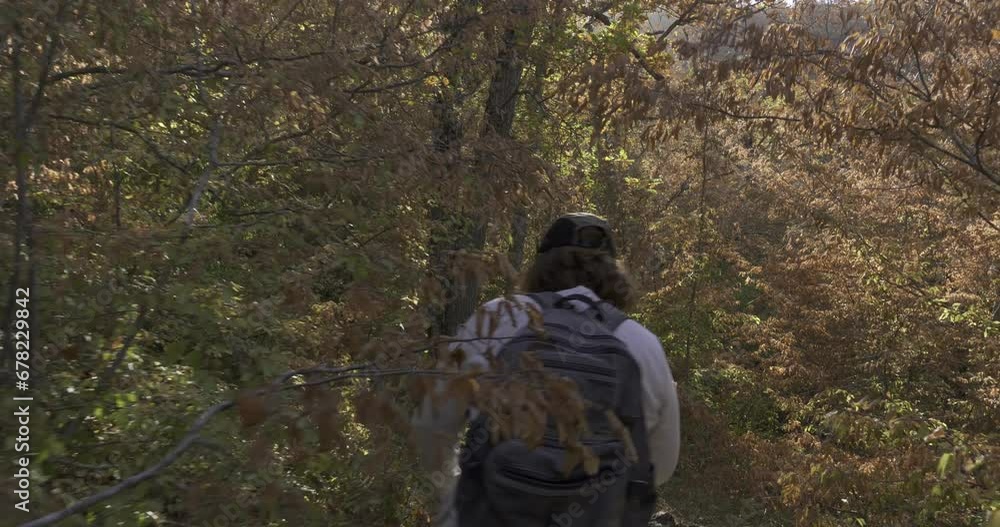 A woman with a backpack walks along a narrow path in a dense autumn forest. Autumn weekend hike. A woman with a backpack walks along a narrow path in a dense autumn forest. Autumn weekend hike.