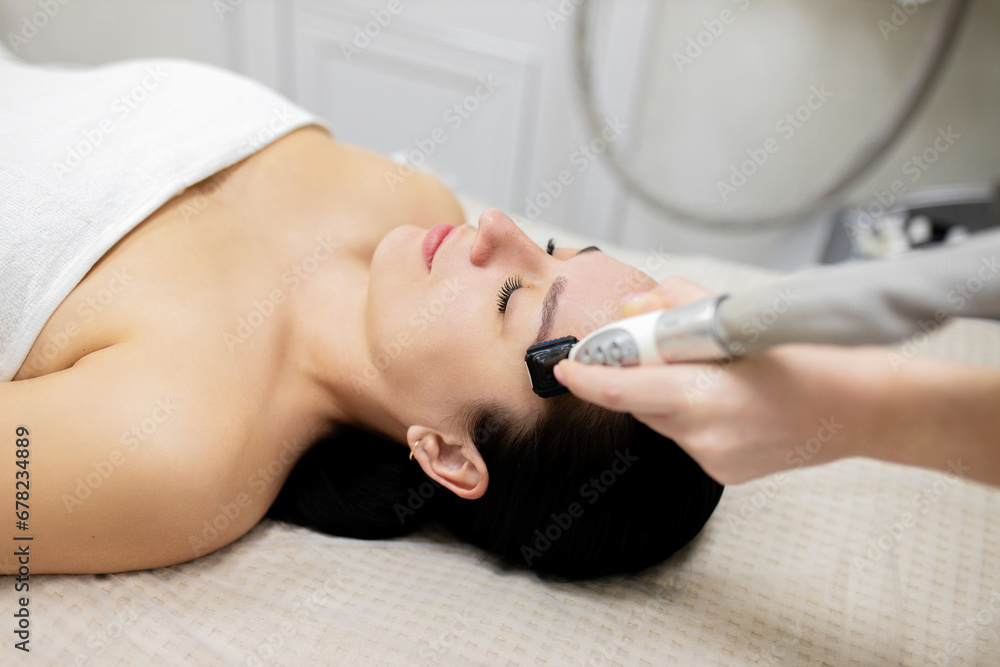 Microneedle RF lifting procedure. Hardware cosmetology. Beautician conducts a facial rejuvenation procedure for a brunette woman Microneedle RF lifting procedure. Hardware cosmetology. Beautician conducts a facial rejuvenation procedure for a brunette woman
