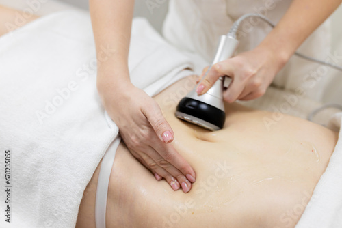 RF body cavitation lifting procedure in a beauty salon. Ultrasound therapy to reduce fat and elasticity of the skin. Cosmetic ultrasonic anti-cellulite massage close-up photo