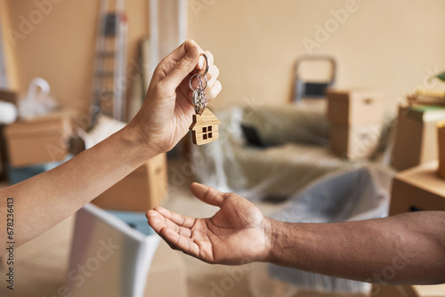 Hand of young female real estate agent passing keys to male owner of new apartment or house in front of camera against living room interior photo