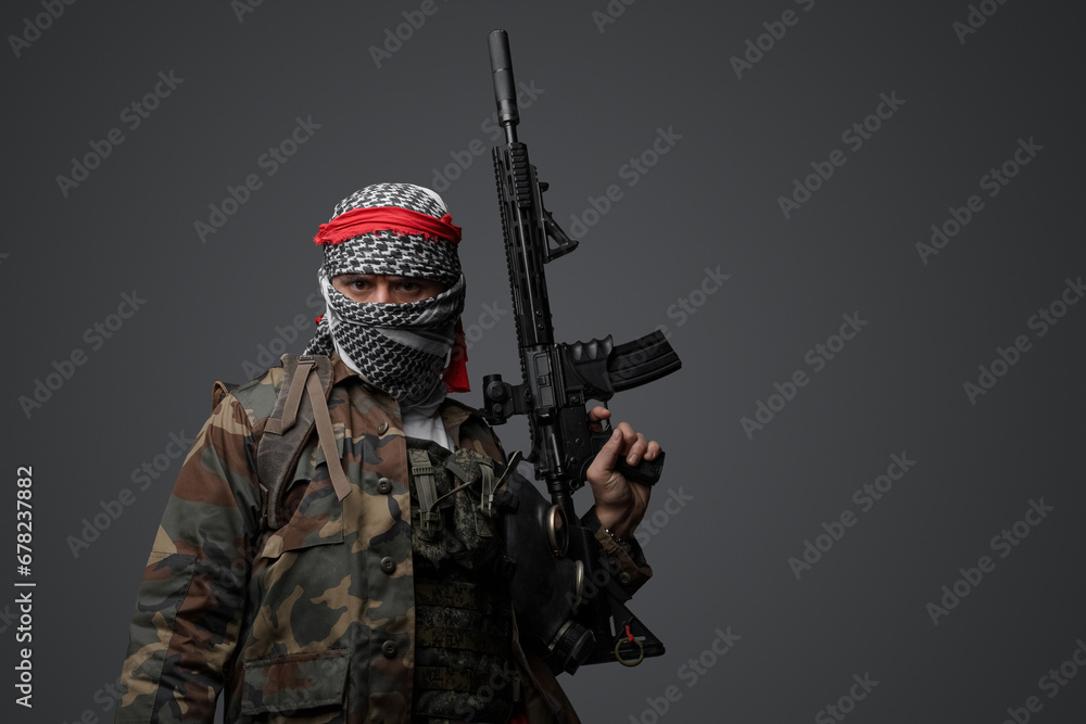 Militant from the Middle East, dressed in a white keffiyeh and camouflaged field attire, wielding an automatic rifle, set against a neutral gray backdrop