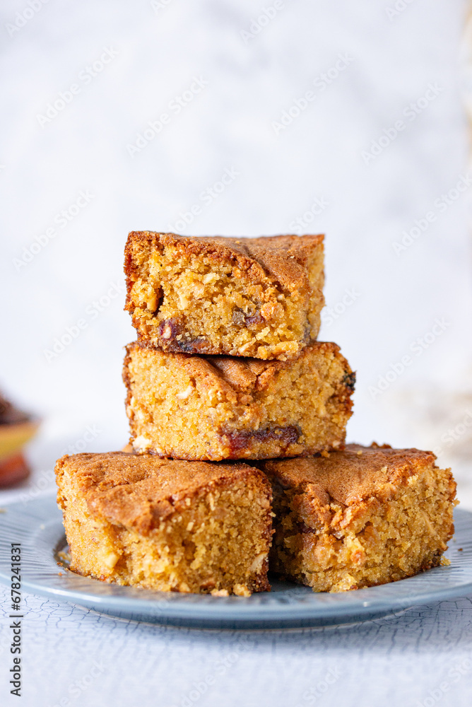 a pile of stacked slices of brown sugar cashew blondies, a vegetarian and vegan dessert with dates, dried fruits on a white background table and plate a pile of stacked slices of brown sugar cashew blondies, a vegetarian and vegan dessert with dates, dried fruits on a white background table and plate