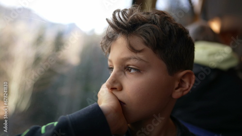Melancholic young boy sitting by train window looking at view with hand in chin, thoughtful pensive expression of pre-teen child traveling and daydreaming photo