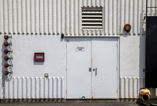 Exterior white steel doors leading to a building sprinkler room, preformed concrete wall panels, fire department annunciator panel and standpipes, daytime, nobody