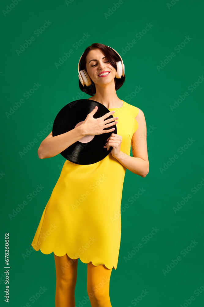 Portrait of young attractive woman dressed style yellow outfit dancing with retro plate while listening music in headphones isolated green background. Portrait of young attractive woman dressed style yellow outfit dancing with retro plate while listening music in headphones isolated green background.