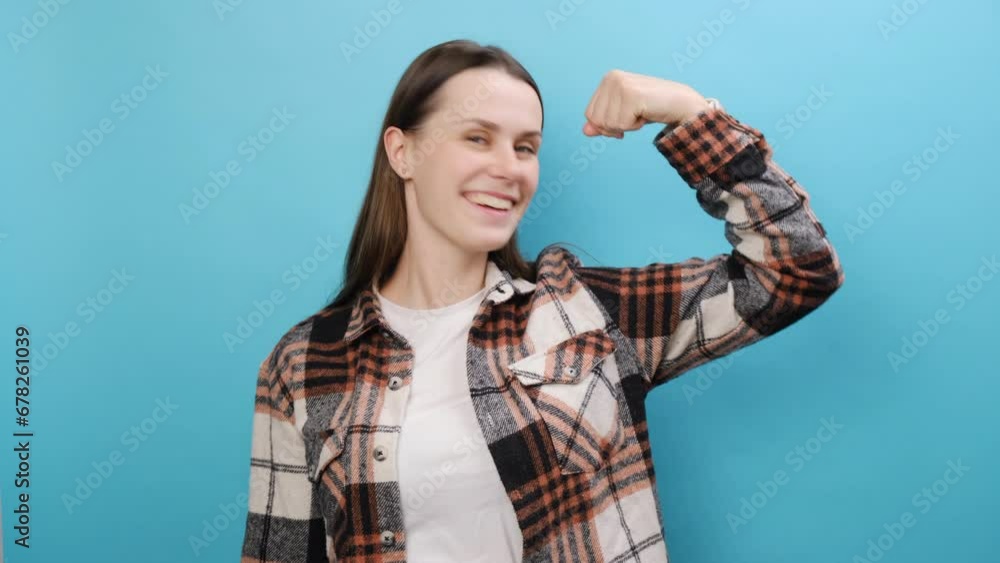 Strong fitness young woman wear casual shirt, showing biceps muscles on hand demonstrating strength power, posing isolated over pastel blue color background wall in studio. People lifestyle concept Strong fitness young woman wear casual shirt, showing biceps muscles on hand demonstrating strength power, posing isolated over pastel blue color background wall in studio. People lifestyle concept