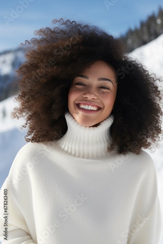 A pretty girl in a white sweater laughs against the backdrop of snowy mountains. Winter vacation, vacation in the mountains.