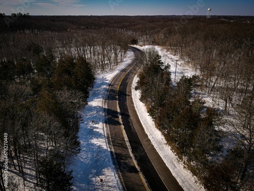 Aerial view of an asphalt road in a forest in winter surrounded by trees © Wirestock