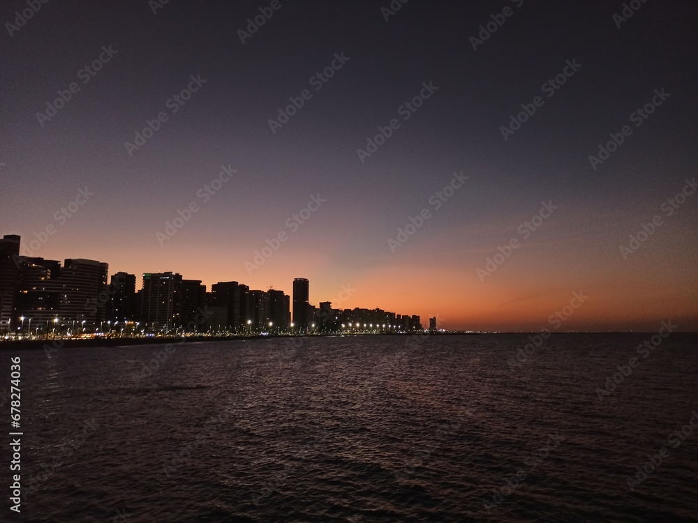 Beachfront twilight in Fortaleza; city lights and azure waves under a soft pink sky