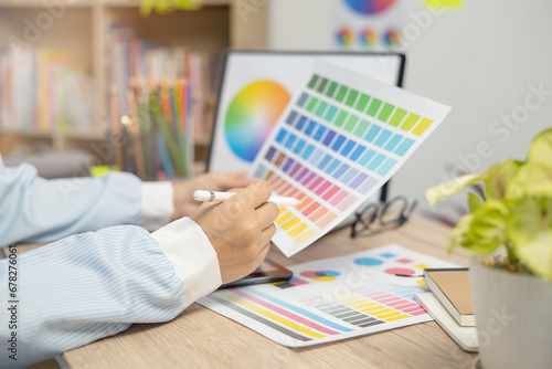 Designer at work on a table, selecting color shades for creative graphic design with laptop