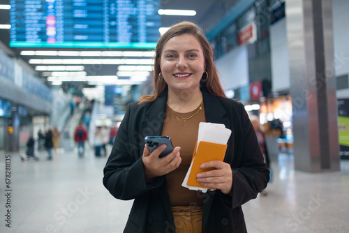 Woman reading phone messages in airport. Happy female buying e-ticket, making hotel reservations and checking in online, holding passport with tickets and carrying suitcase while departing departure 