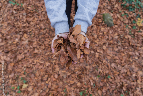 Woman holding leaves between her hands over background of more fallen autumnal leaves at 