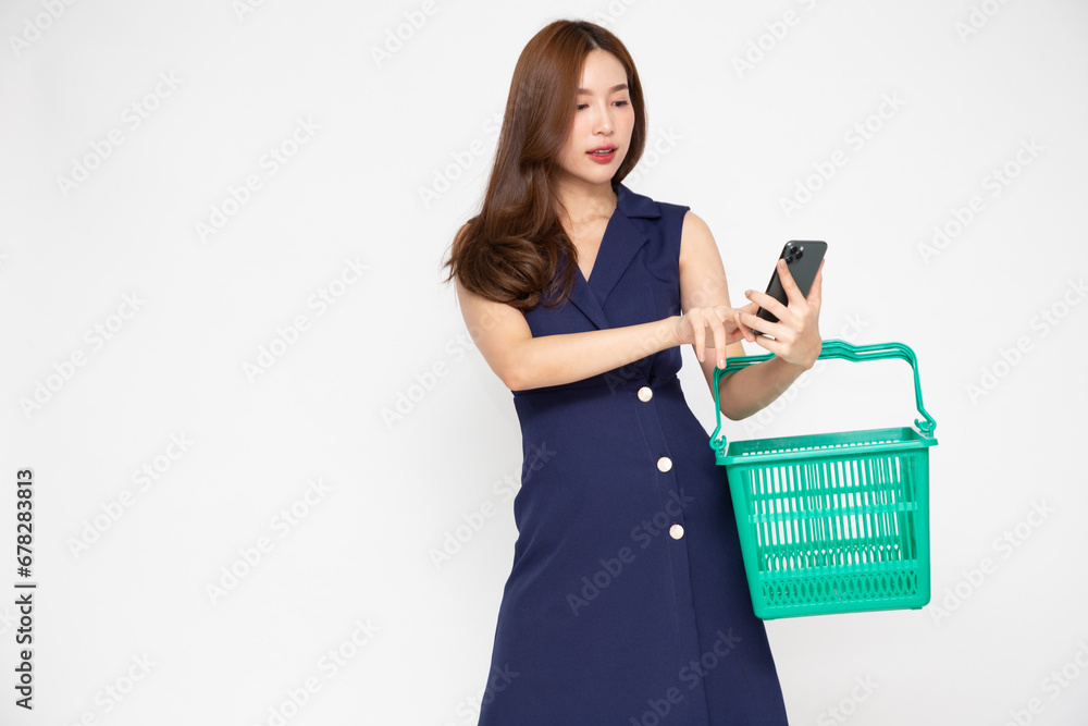 Young Asian woman smiling and holding shopping basket and using mobile phone application isolated on white background Young Asian woman smiling and holding shopping basket and using mobile phone application isolated on white background