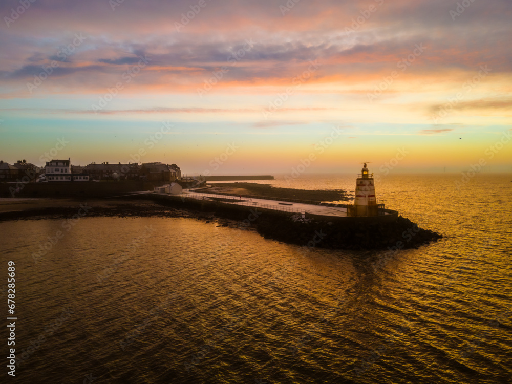 a large white lighthouse is on the water at sunset and sits in the foreground