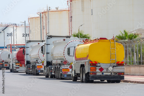 Parking row jam of trucks with fuel tanks in front of a warehouse and storage of huge tanks of raw material containers.