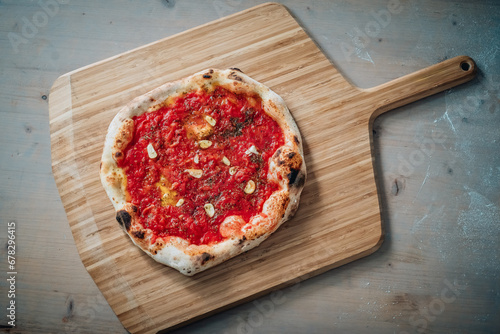 Pizza marinara al pomodoro e aglio appena cotta offerta su una pala di legno di un pizzaiolo photo