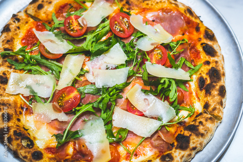 Neapolitan style pizza with cheese, patma ham, arugula, tomato sauce and cherry tomatoes