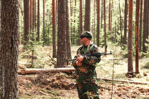 Russian soldier man in military camouflage uniform with weapon on war standing at forest background. Military male border guard in country border holding machine gun at nature. Copy ad text space