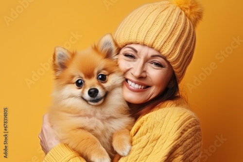 Horizontal shot of happy Afro American hostess poses with cute spitz puppy with stucked out tongue, looks aside and smiles, have nice walk together, isolated on yellow background, blank space © Georgii