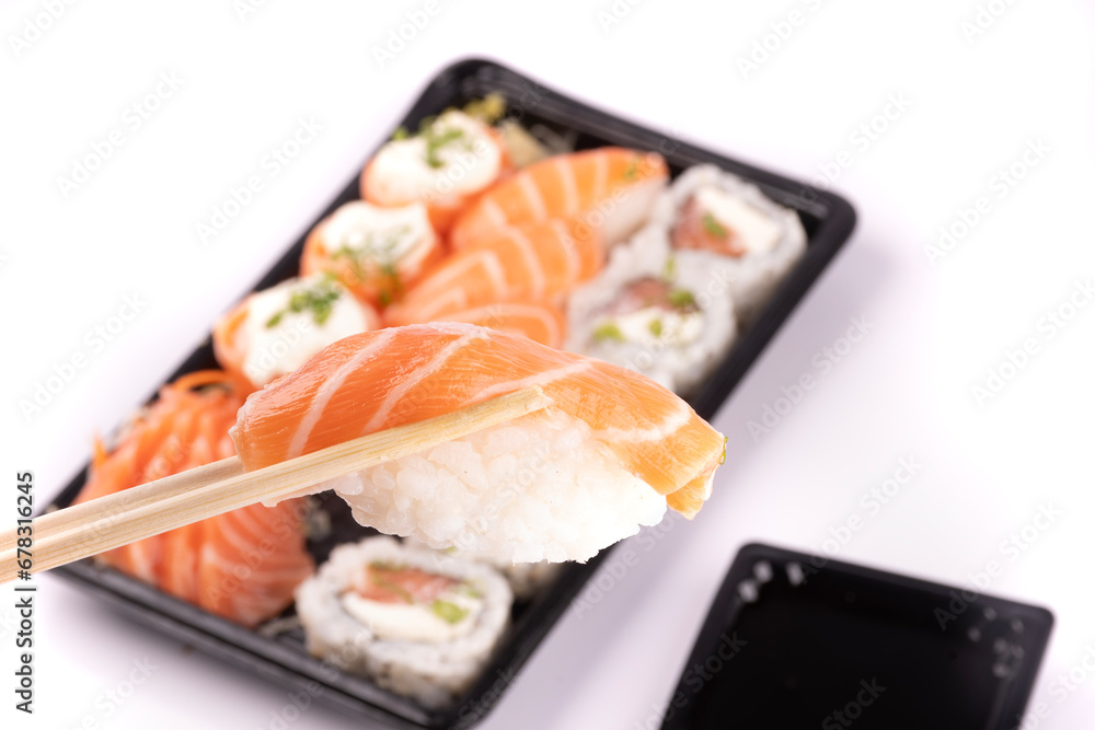 holding a piece of nigiri with chopsticks and blurred sushi tray in the background holding a piece of nigiri with chopsticks and blurred sushi tray in the background